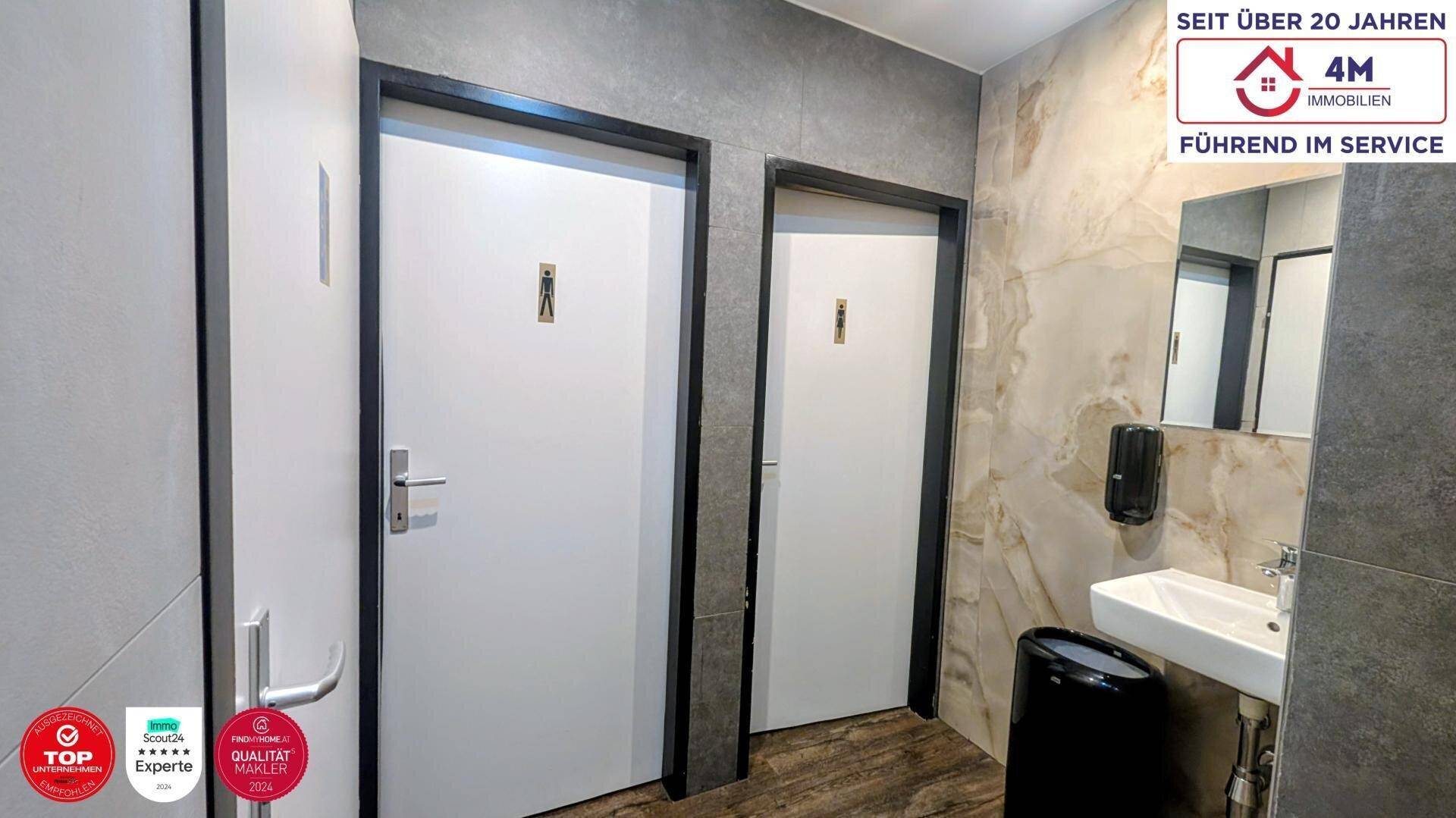 Eingangsbereich zu den Toiletten mit zwei Türen, Waschbecken und Spiegel in modernem Design.