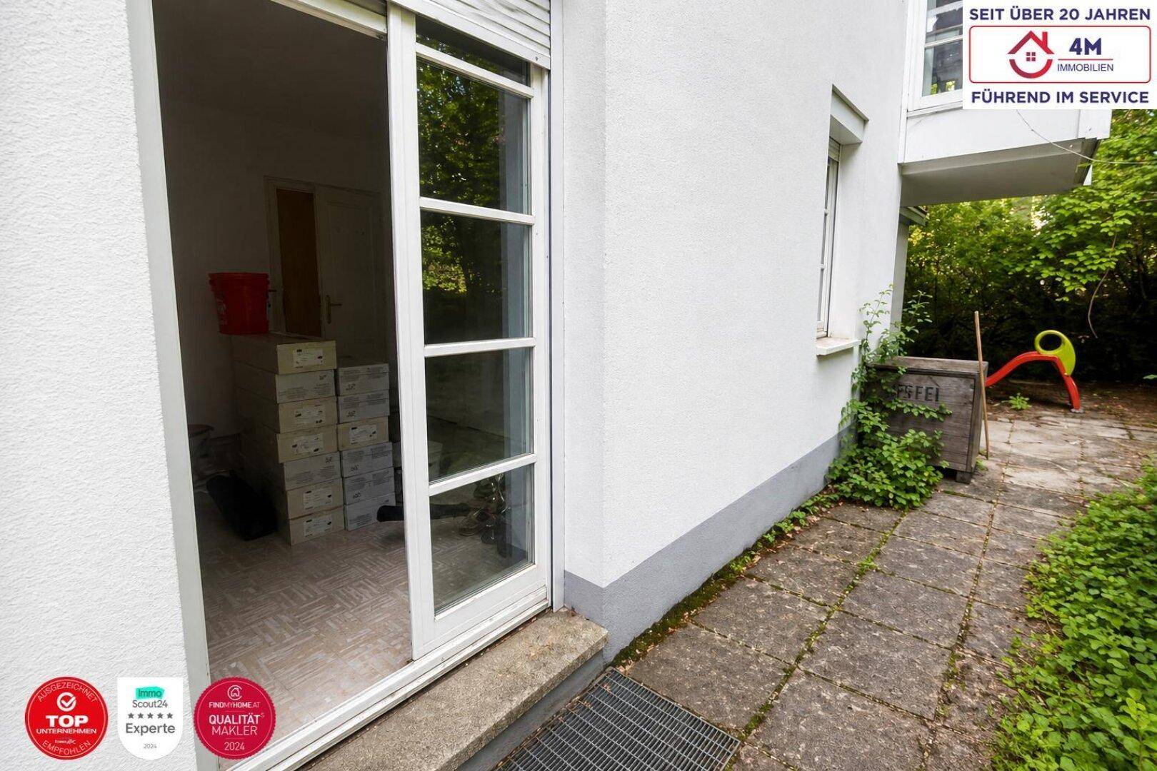 Ausgang zum Außenbereich mit gepflastertem Weg und Blick ins Grüne, dahinter ein Abstellraum.