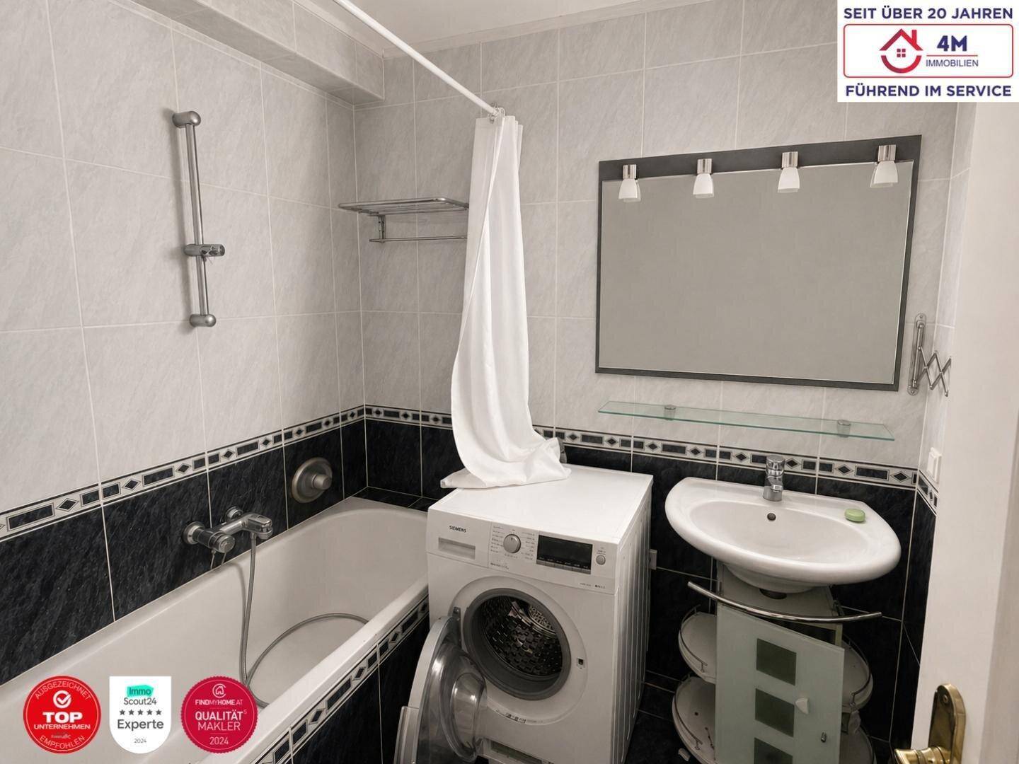 Badezimmer mit Badewanne, Waschbecken, Spiegel und Waschmaschine, modern gefliest.