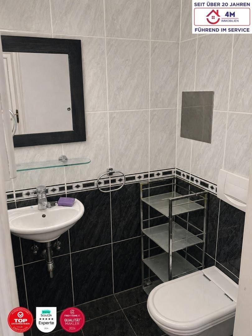 Modern gefliestes Gäste-WC mit Waschbecken, Spiegel und Wand-WC.