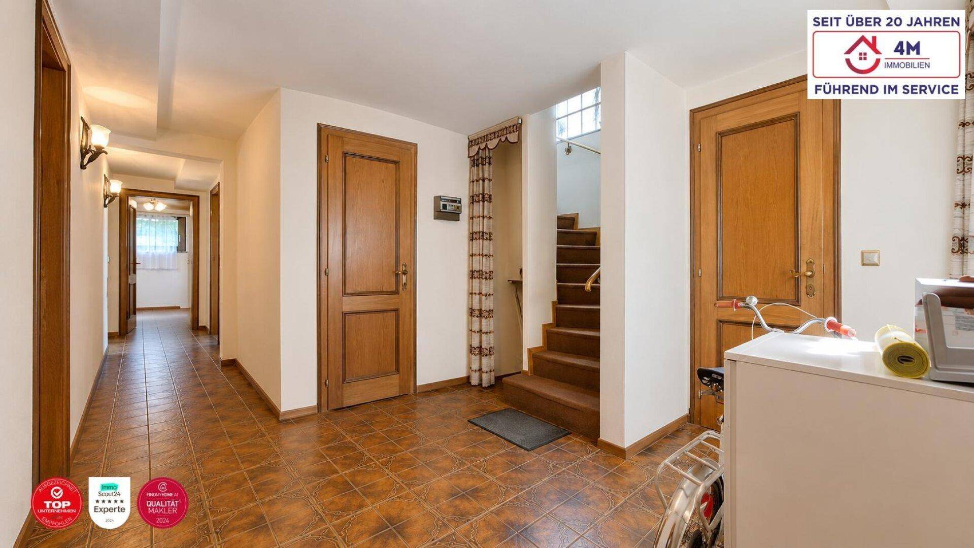 Langer Flur mit Fliesenboden, Holztüren und Zugang zu verschiedenen Räumen und einer Treppe.
