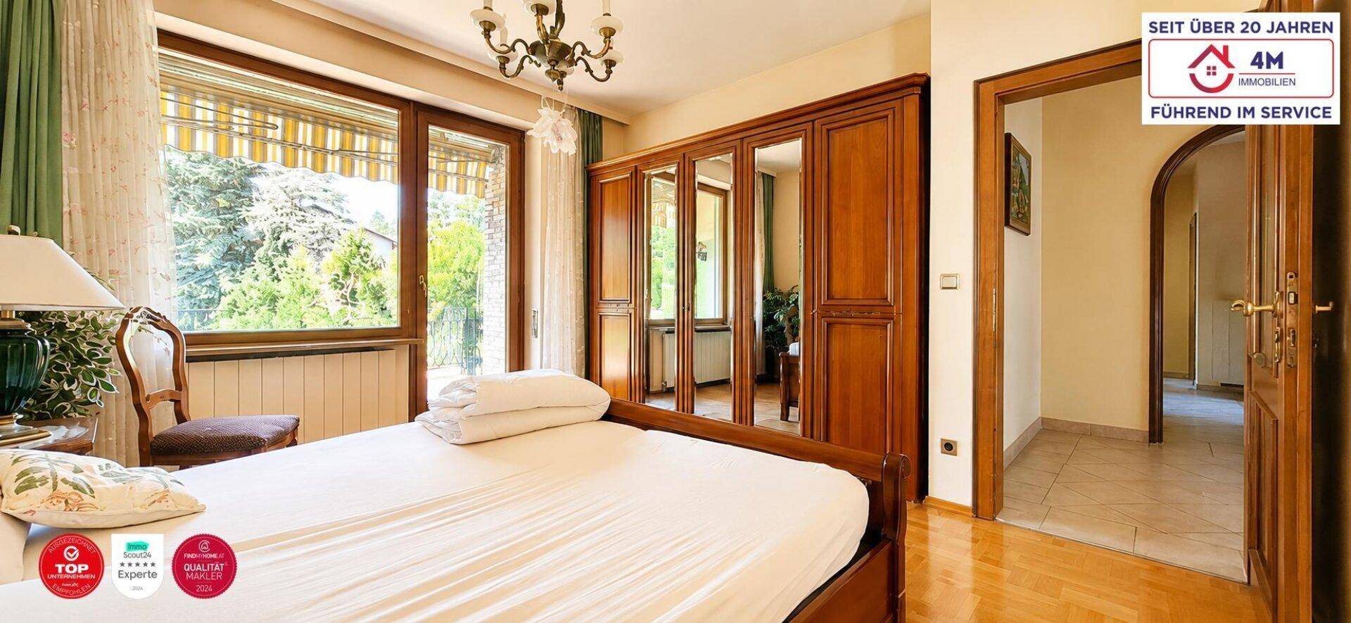 Geräumiges Schlafzimmer mit großem Fenster, Holzkleiderschrank und Blick ins Grüne.