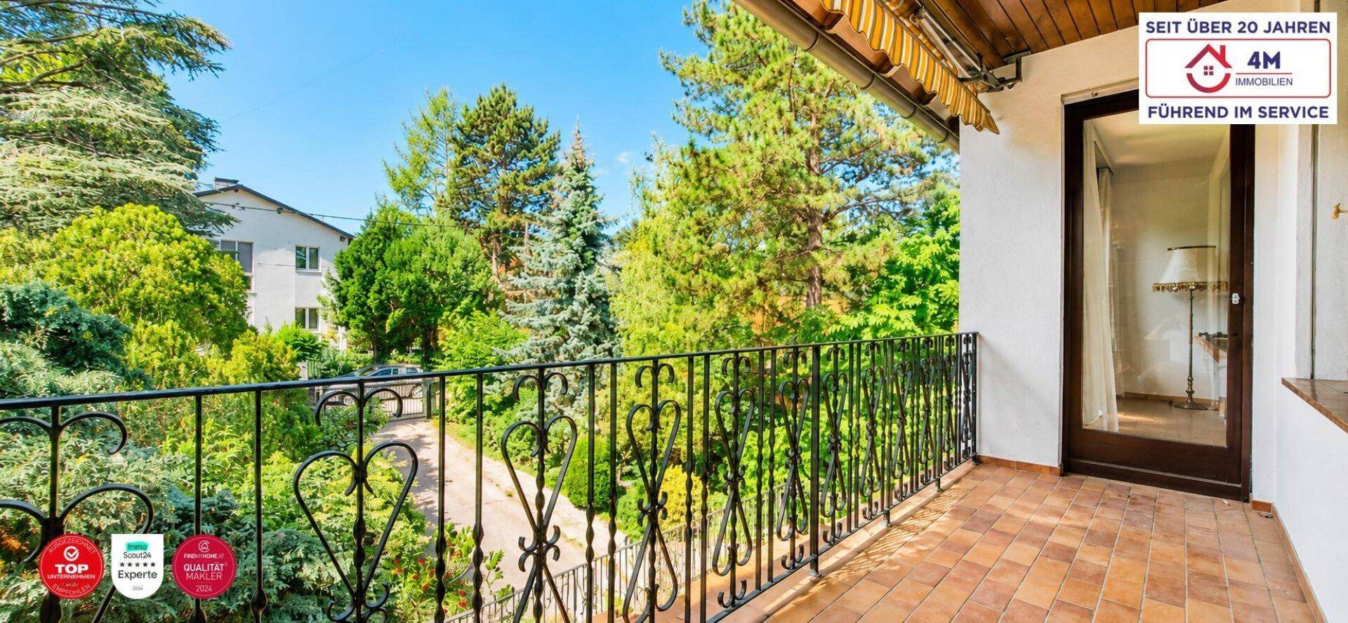 Sonniger Balkon mit schmiedeeisernem Geländer und weitem Blick in die grüne Umgebung.