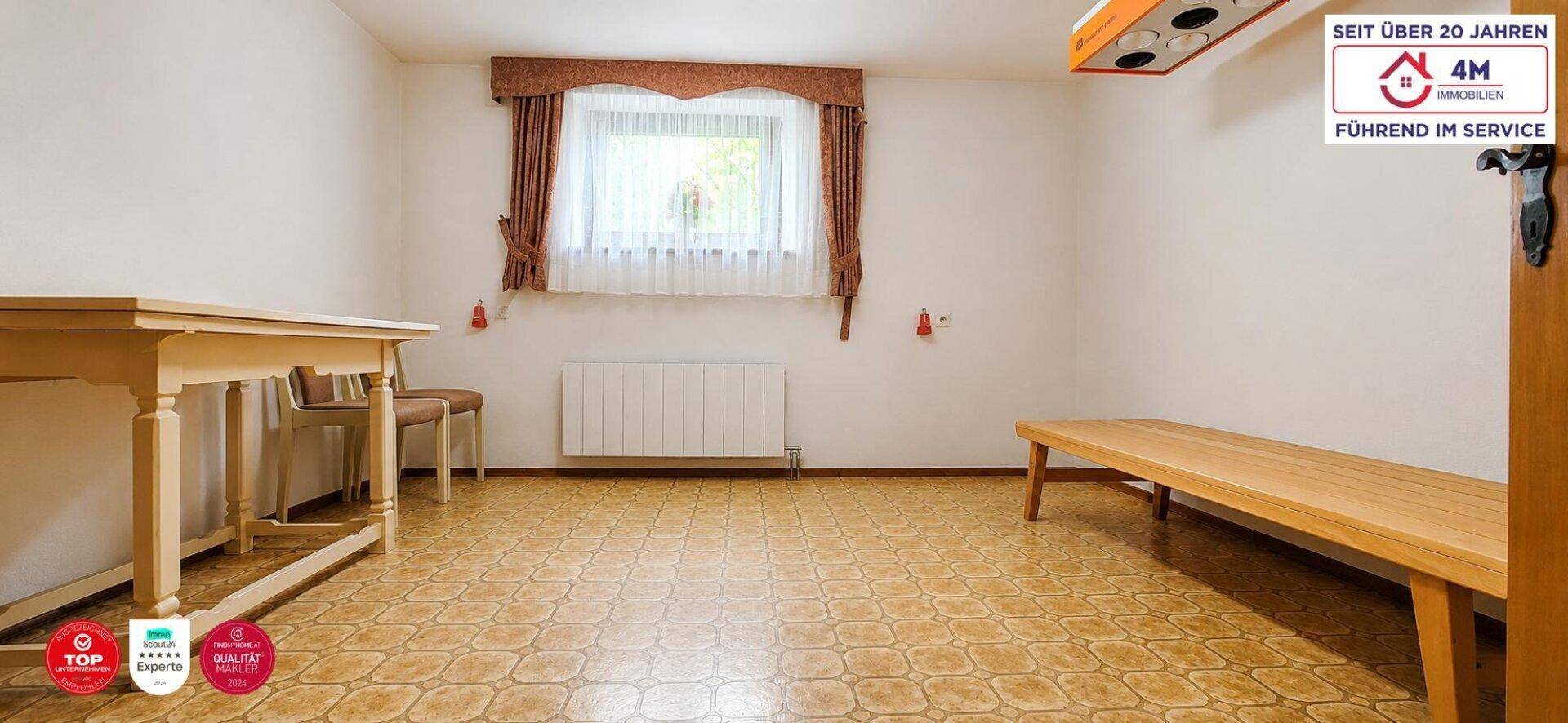 Heller Raum mit Fliesenboden, großem Fenster und einfacher Einrichtung.