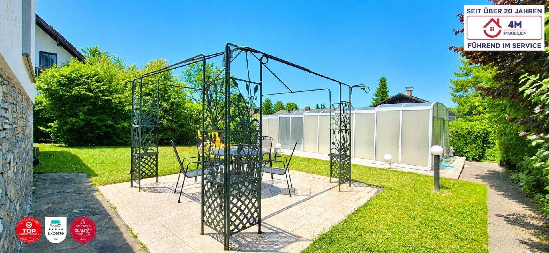 Sonniger Gartenbereich mit einem dekorativen Pavillon und einem Gewächshaus im Hintergrund.