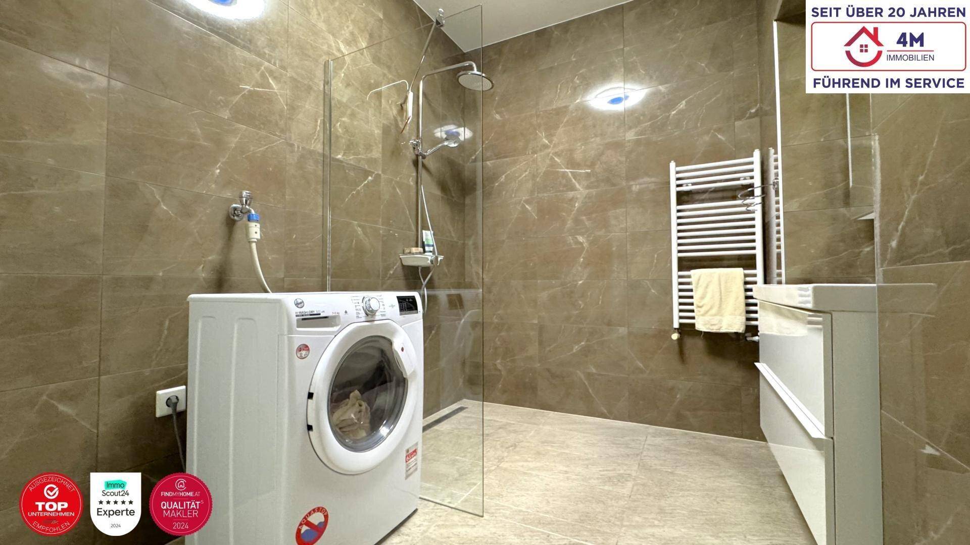 Modernes Badezimmer mit braunen Fliesen, ebenerdiger Dusche, Waschmaschine und beheiztem Handtuchhalter.