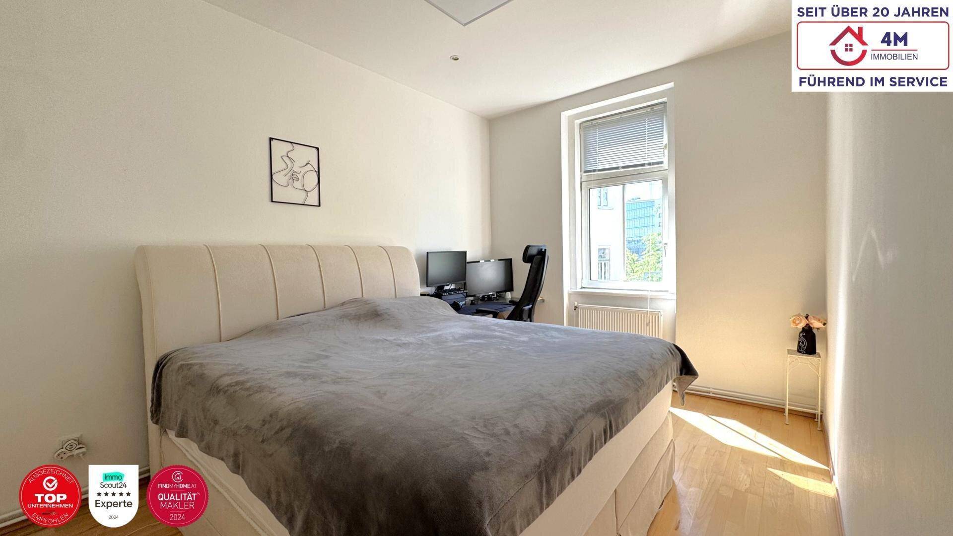 Schlafzimmer mit großem Bett, Holzboden und einem Fenster, das viel Tageslicht hereinlässt.