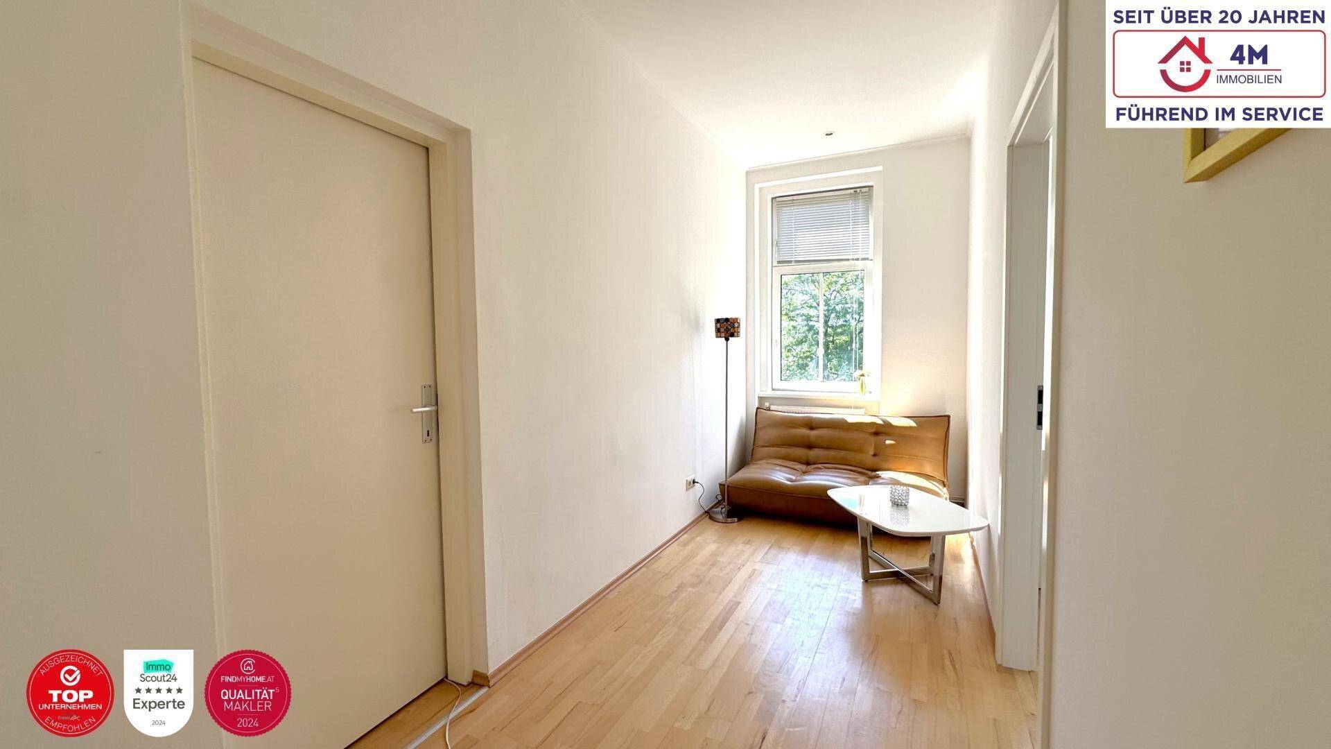 Helles Wohnzimmer mit Holzboden, kleiner Couch und einem Fenster mit Blick ins Grüne.