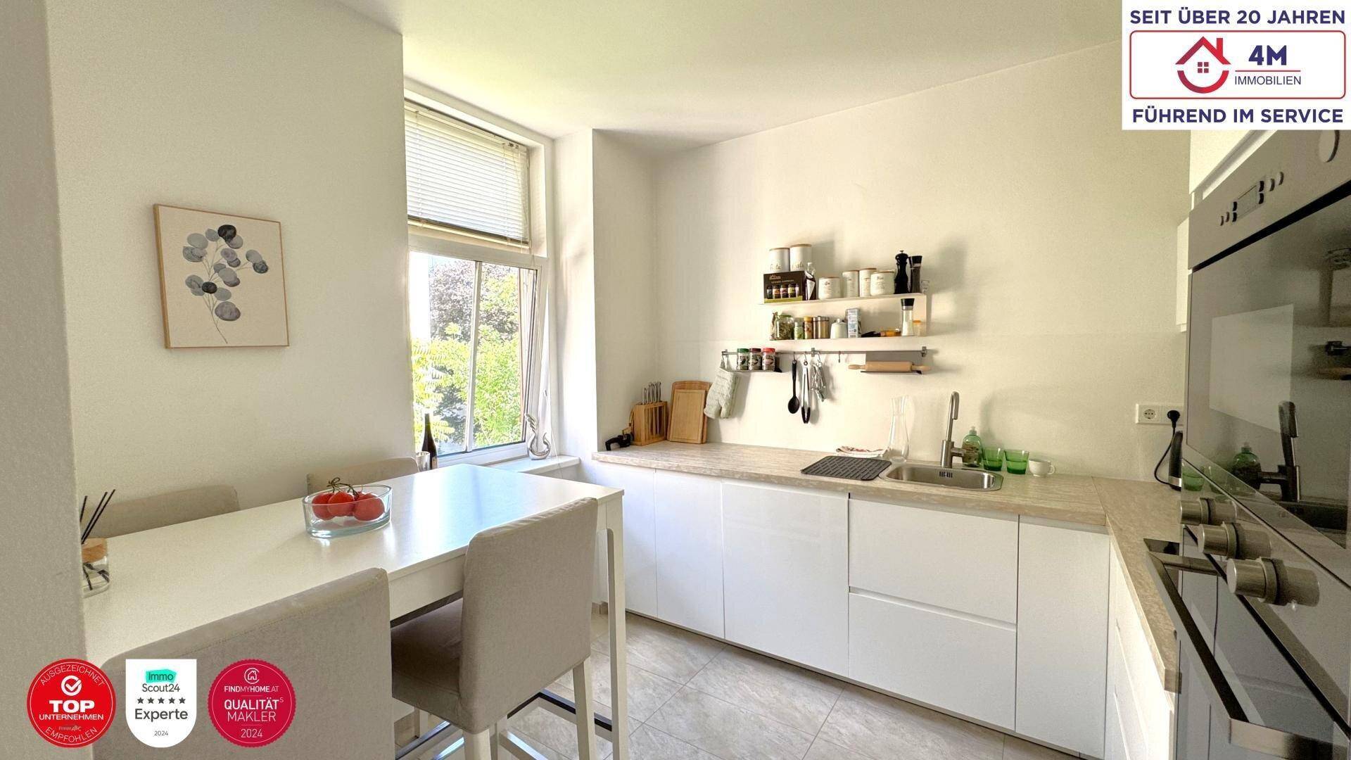 Moderne weiße Küche mit Essbereich, Fenster und Blick ins Grüne, ausgestattet mit Einbaugeräten.
