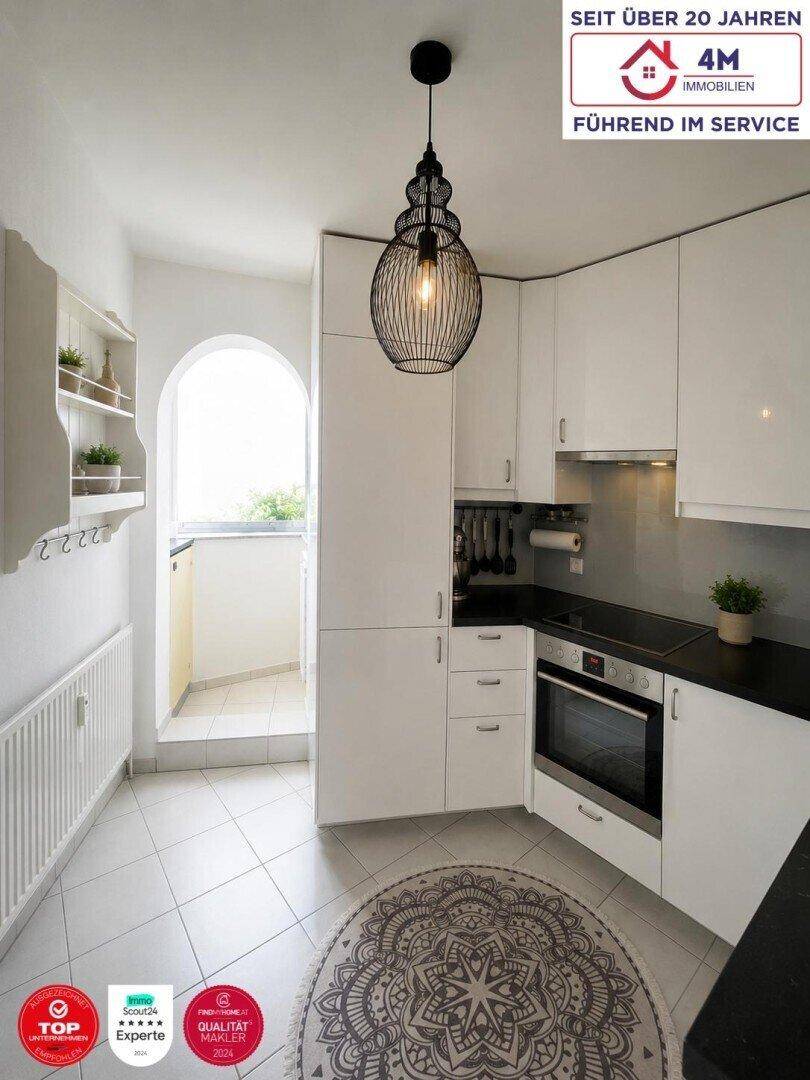 Moderne Einbauküche mit weißen Schränken, dunkler Arbeitsplatte und Zugang zu einem kleinen Balkon.