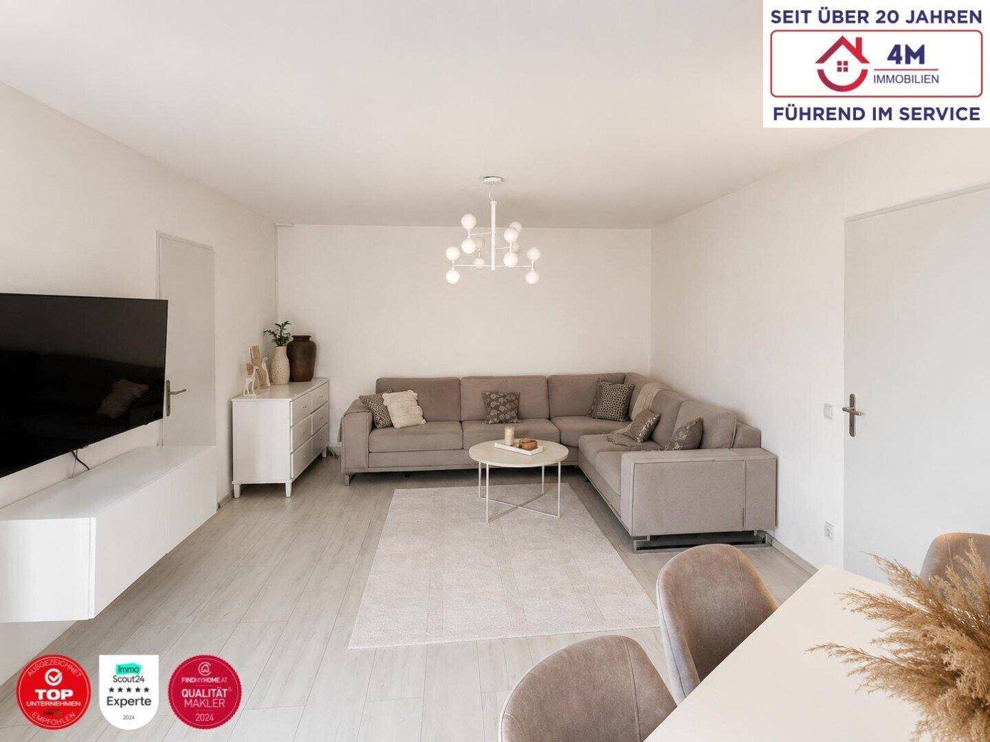 Geräumiger Wohnbereich mit beigem Ecksofa, modernem Kronleuchter und hellem Laminatboden.