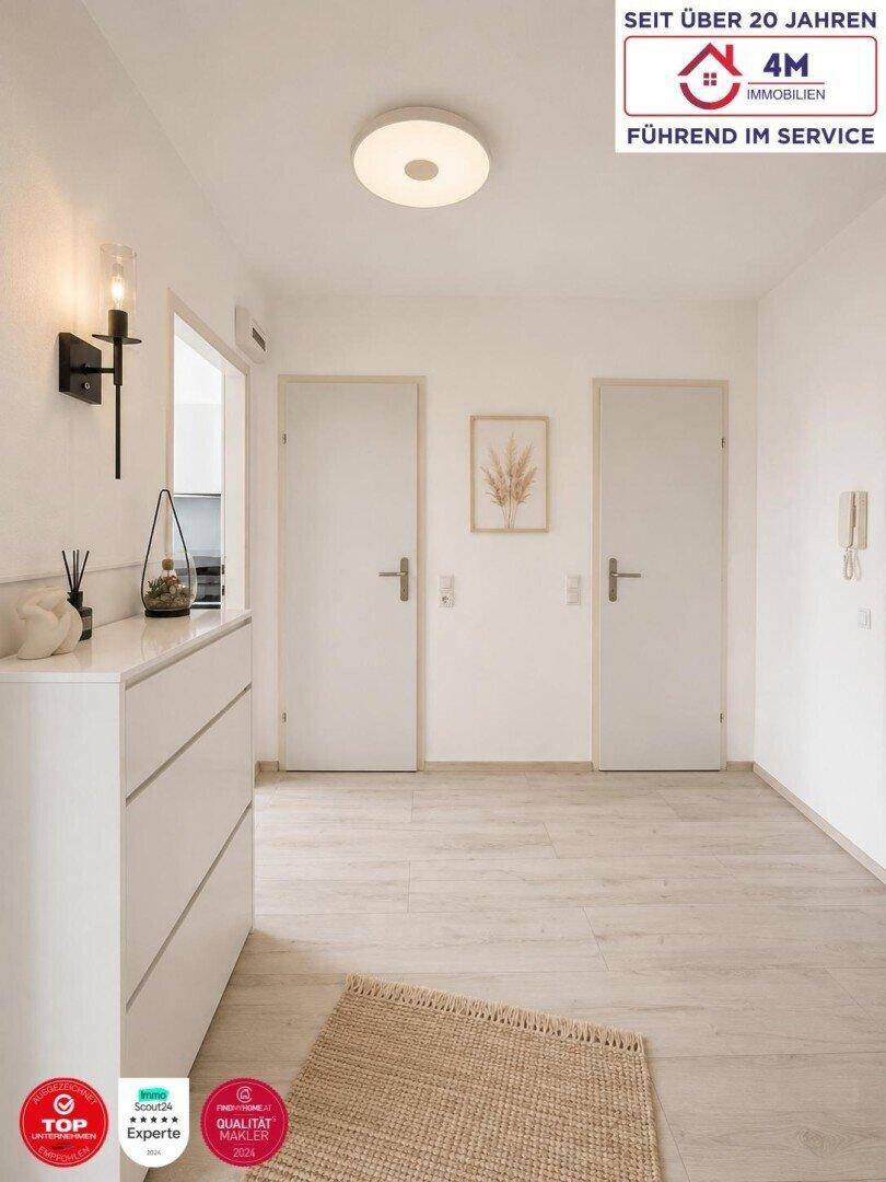 Heller Flur mit weißer Kommode, Wandleuchte und zwei Türen zu weiteren Räumen.