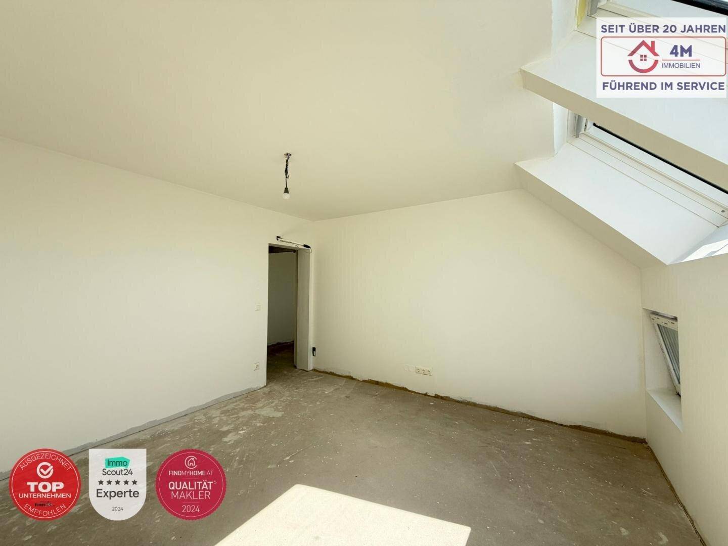 Unfertiger Innenraum mit weißen Wänden, Betonboden und einem Dachfenster, das viel Licht spendet.
