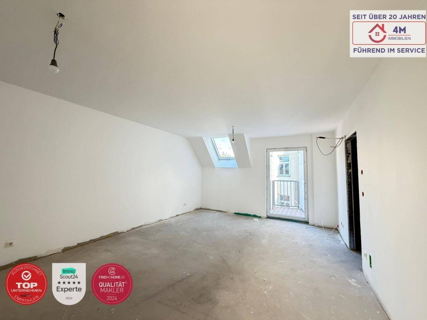 Unfertiger Innenraum mit Zugang zu einem kleinen Balkon und einem weiteren Dachfenster für Helligkeit.