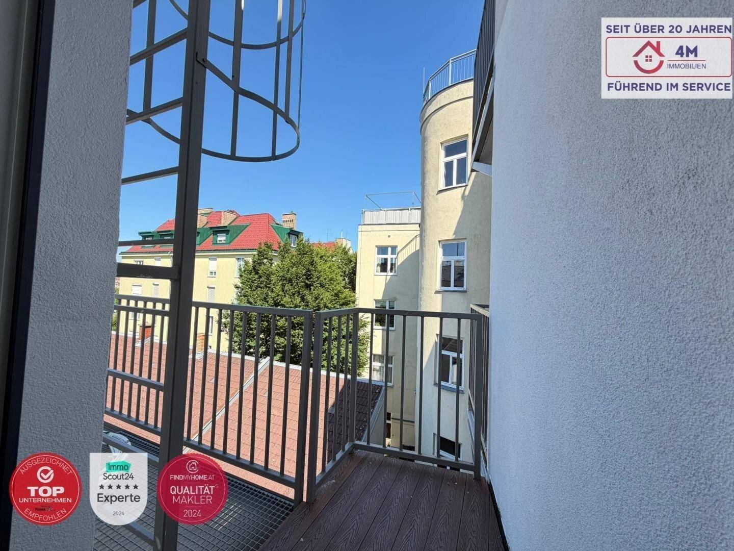 Balkon mit Holzboden und Metallgeländer bietet einen Blick auf die umliegenden Gebäude und Dächer.