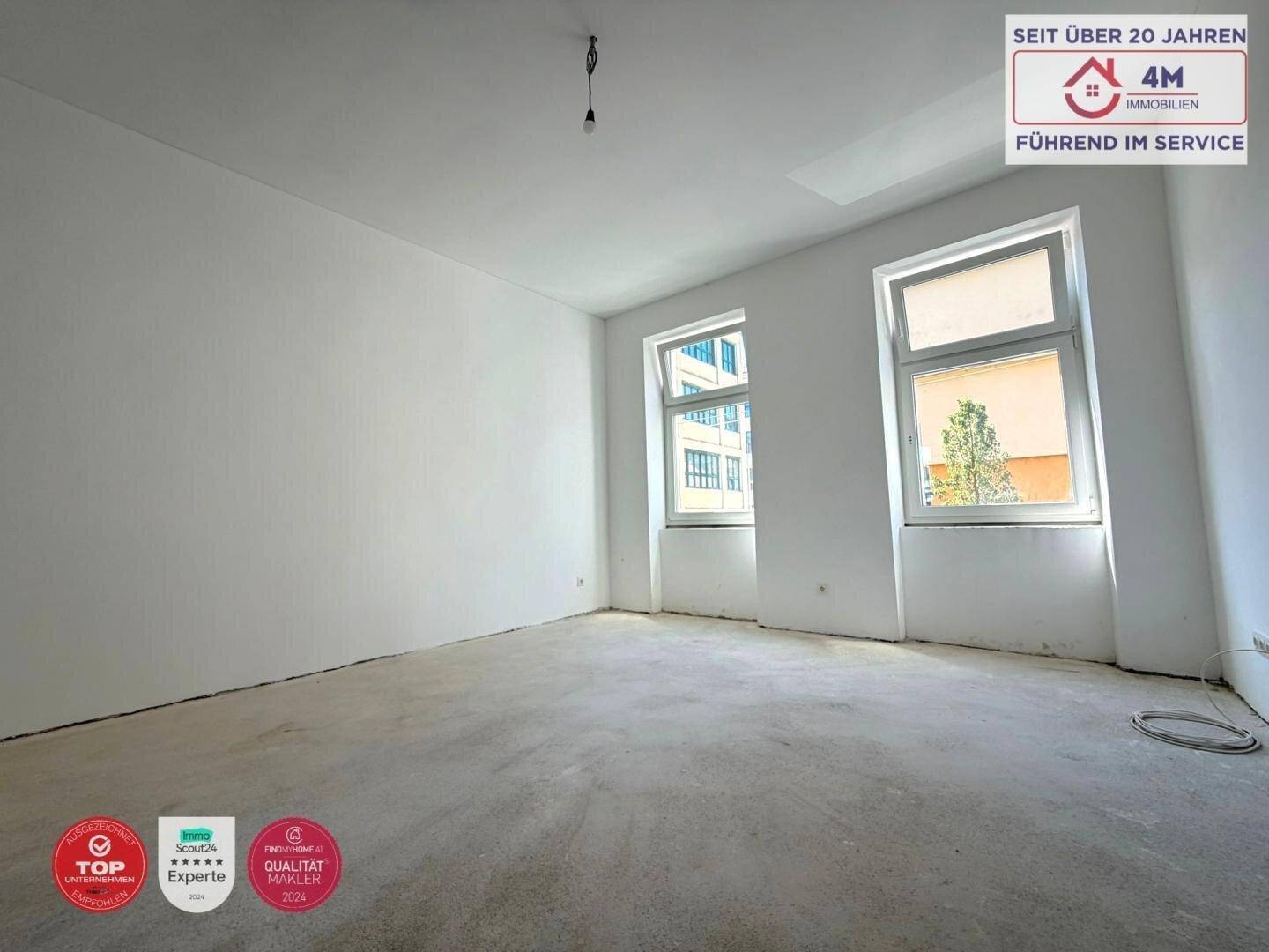 Geräumiger, heller Raum mit großen Fenstern und Betonboden, ideal für zukünftige Wohnnutzung.