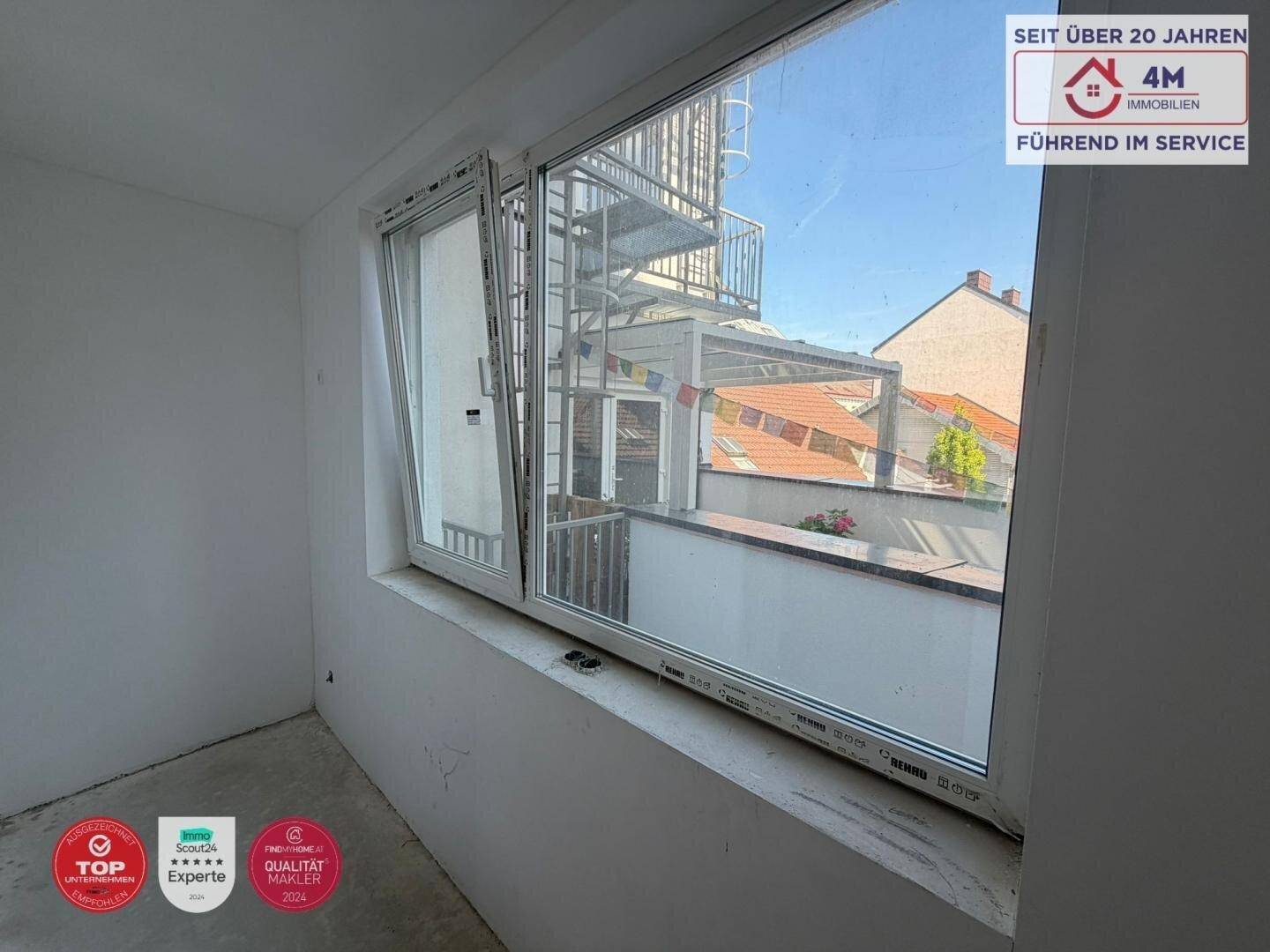 Fensterblick auf eine Außentreppe und umliegende Dächer, der viel Tageslicht in den Raum bringt.