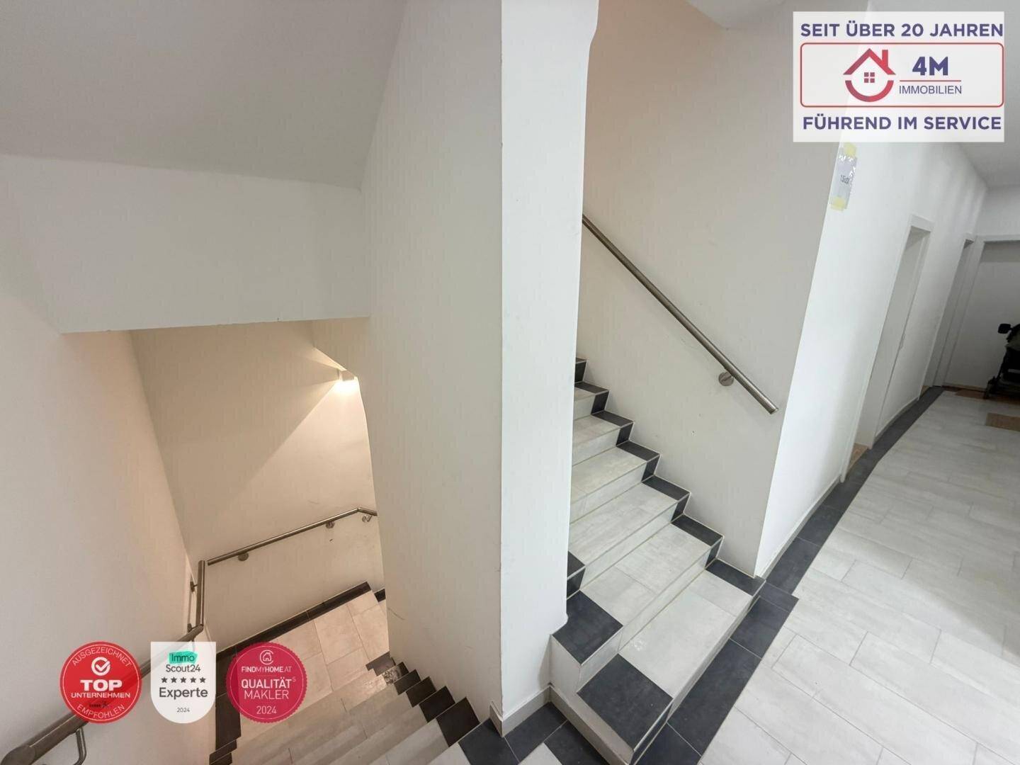 Modernes Treppenhaus mit gefliesten Stufen und Edelstahlgeländer, gut beleuchtet und sicher.