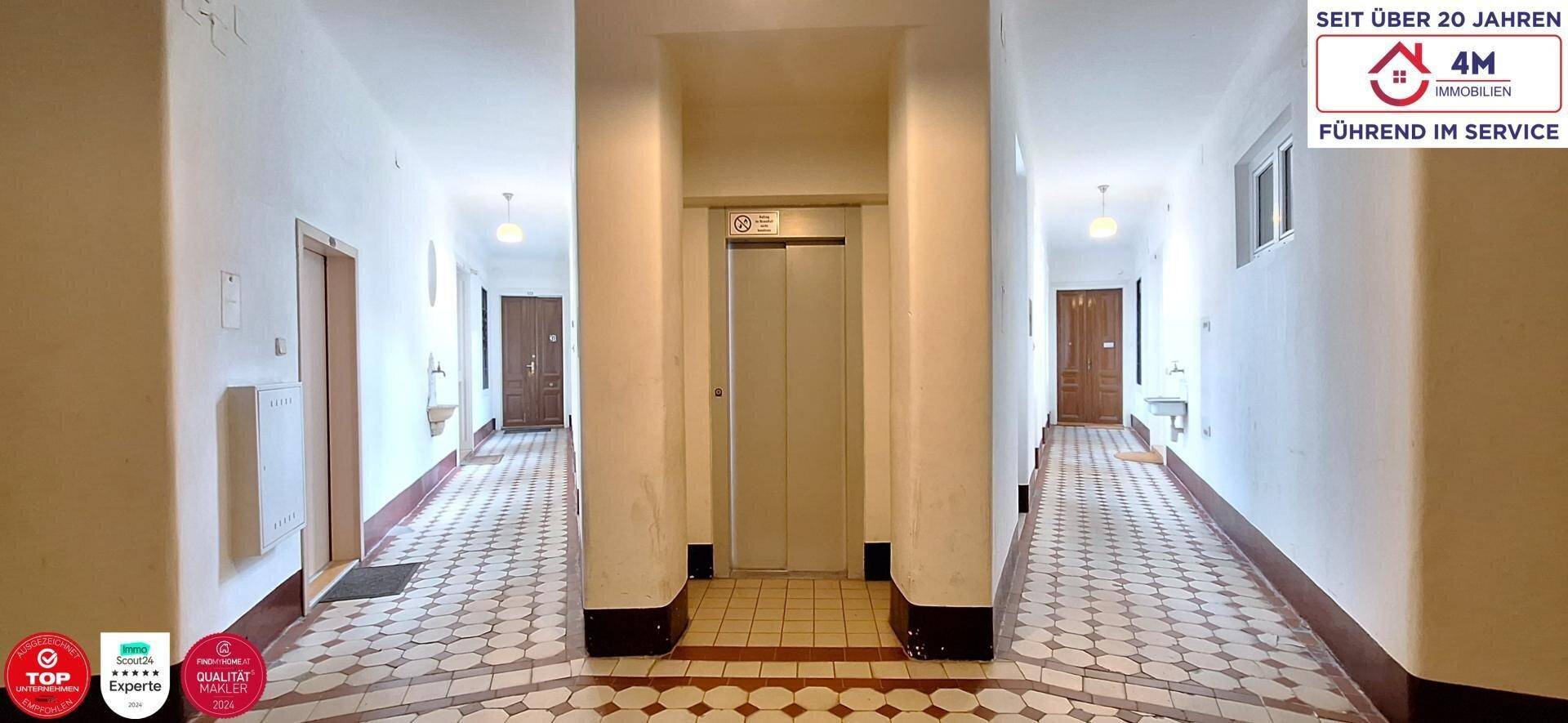 Geräumiger Flur im Gebäude mit Aufzug und traditionellem Fliesenboden.
