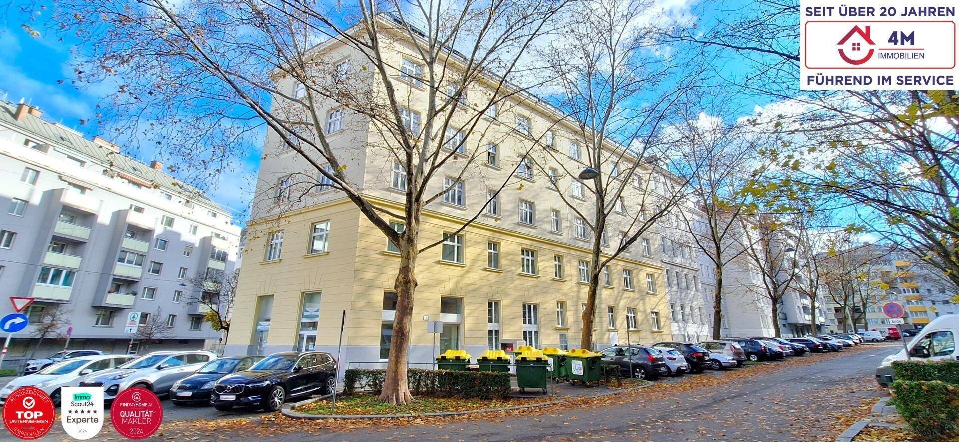 Klassisches Mehrfamilienhaus mit heller Fassade und Bäumen entlang der Straße.