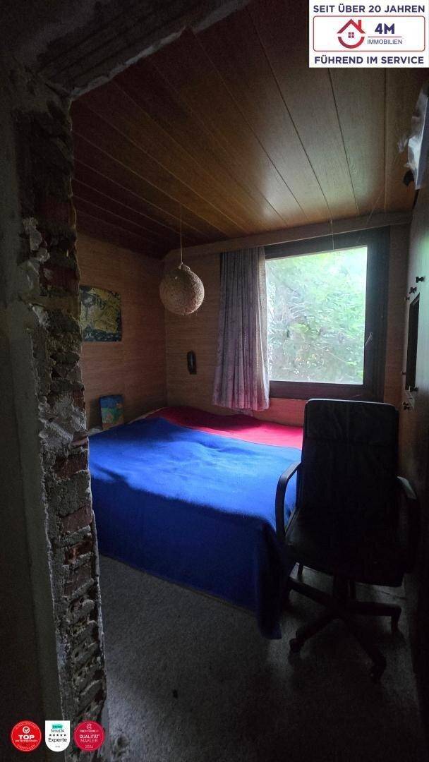 Gemütliches Schlafzimmer mit Bett, Schreibtischstuhl und Fenster, teilweise mit freiliegendem Mauerwerk.
