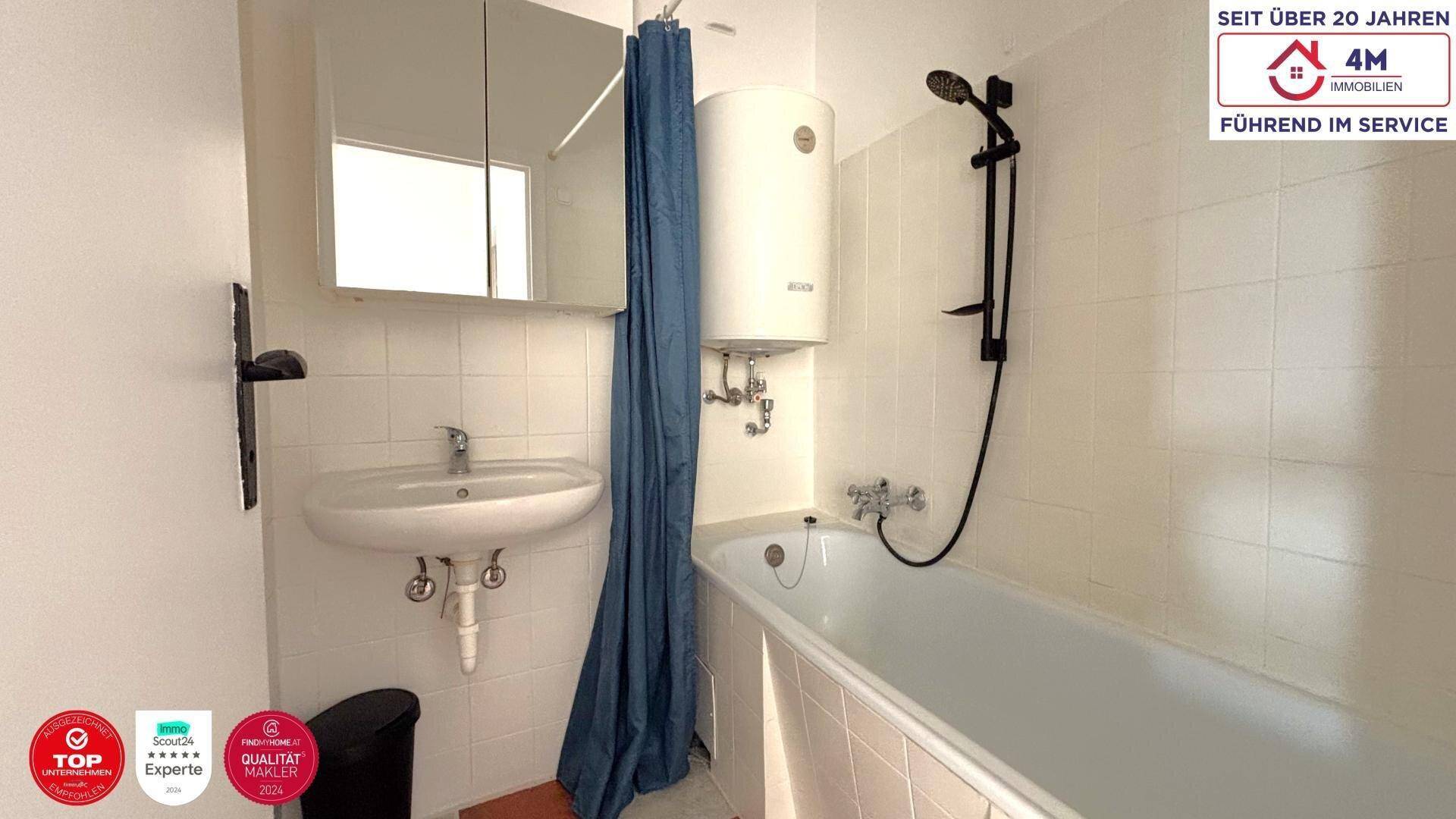 Helles Badezimmer mit Badewanne, Duschvorhang und Spiegelschrank über dem Waschbecken.