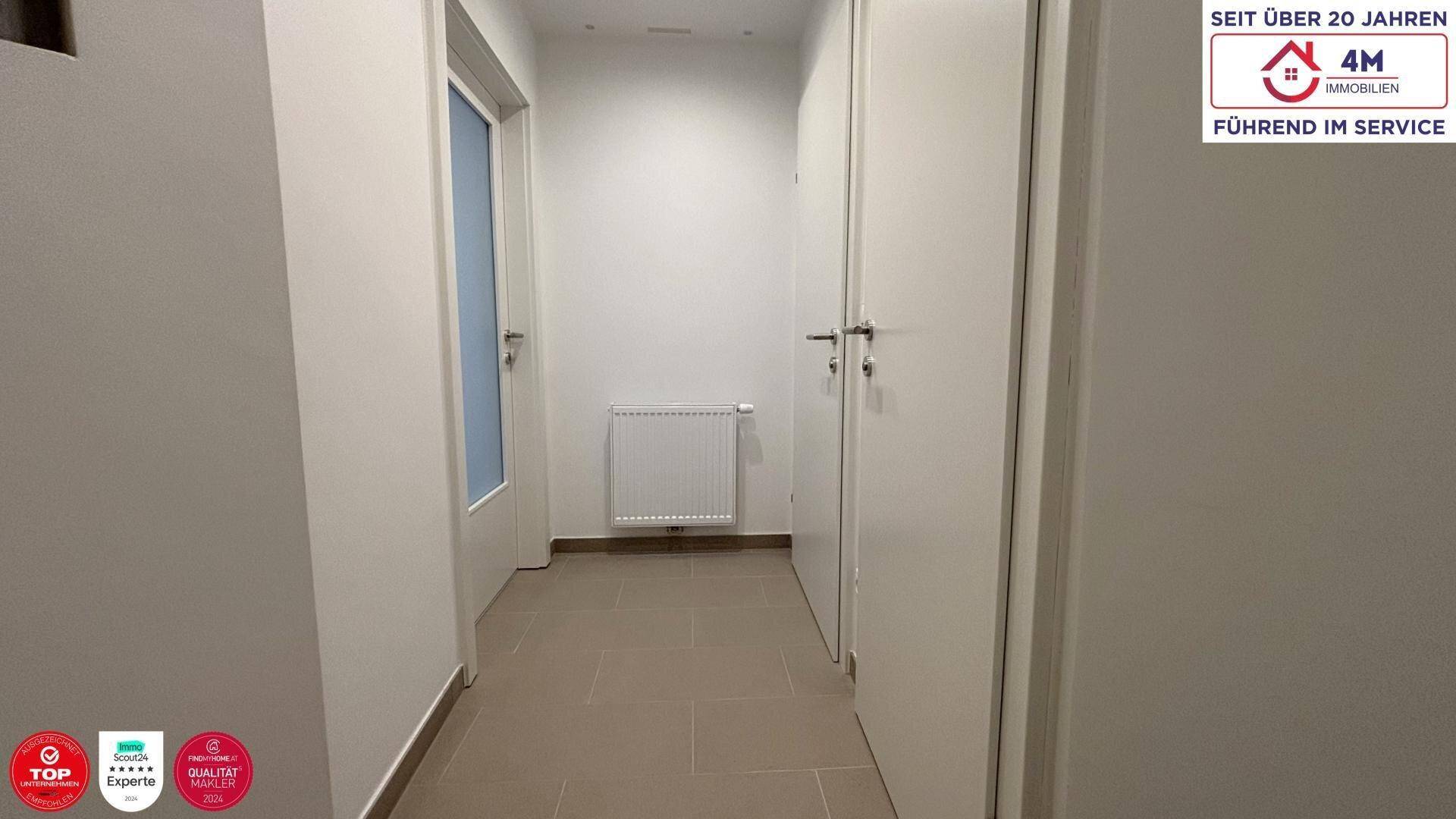Schlichter Flur mit hellen Fliesen und weißen Türen, ausgestattet mit einem Heizkörper.