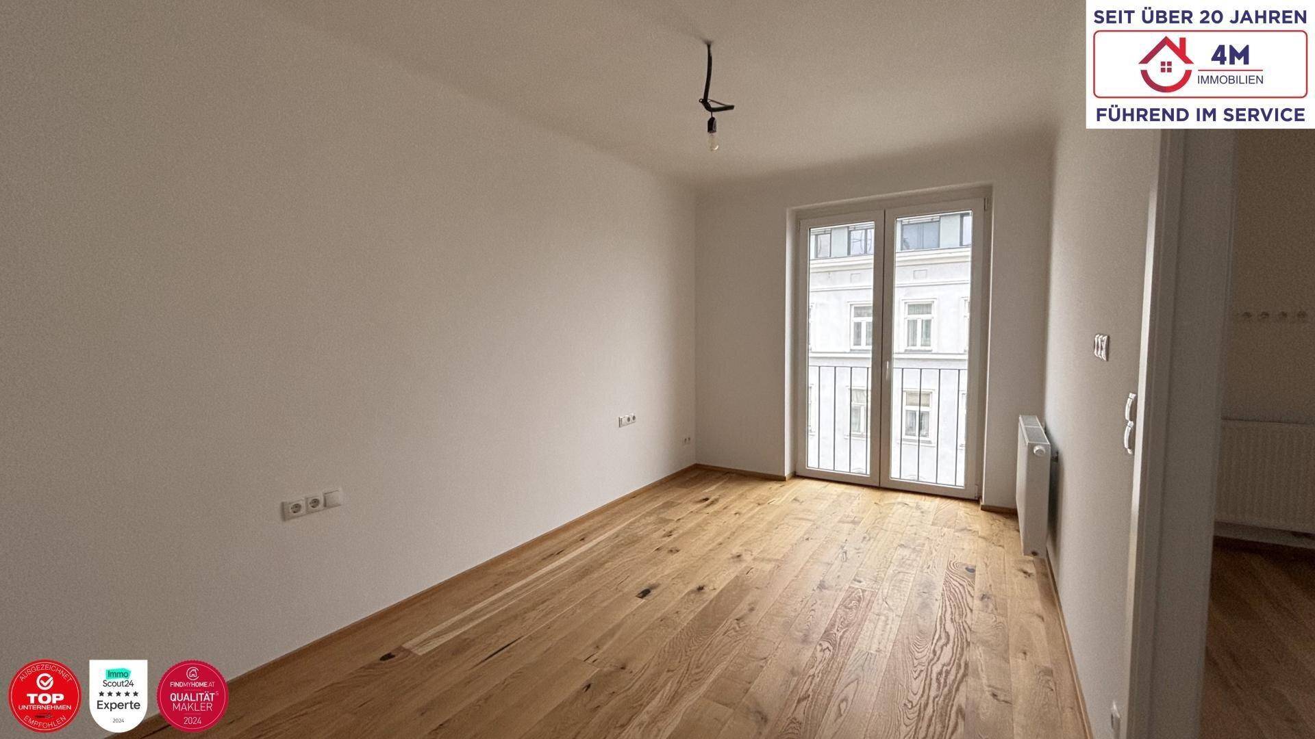 Leerer Raum mit Holzboden und großem Fenster, das viel Tageslicht hereinlässt.
