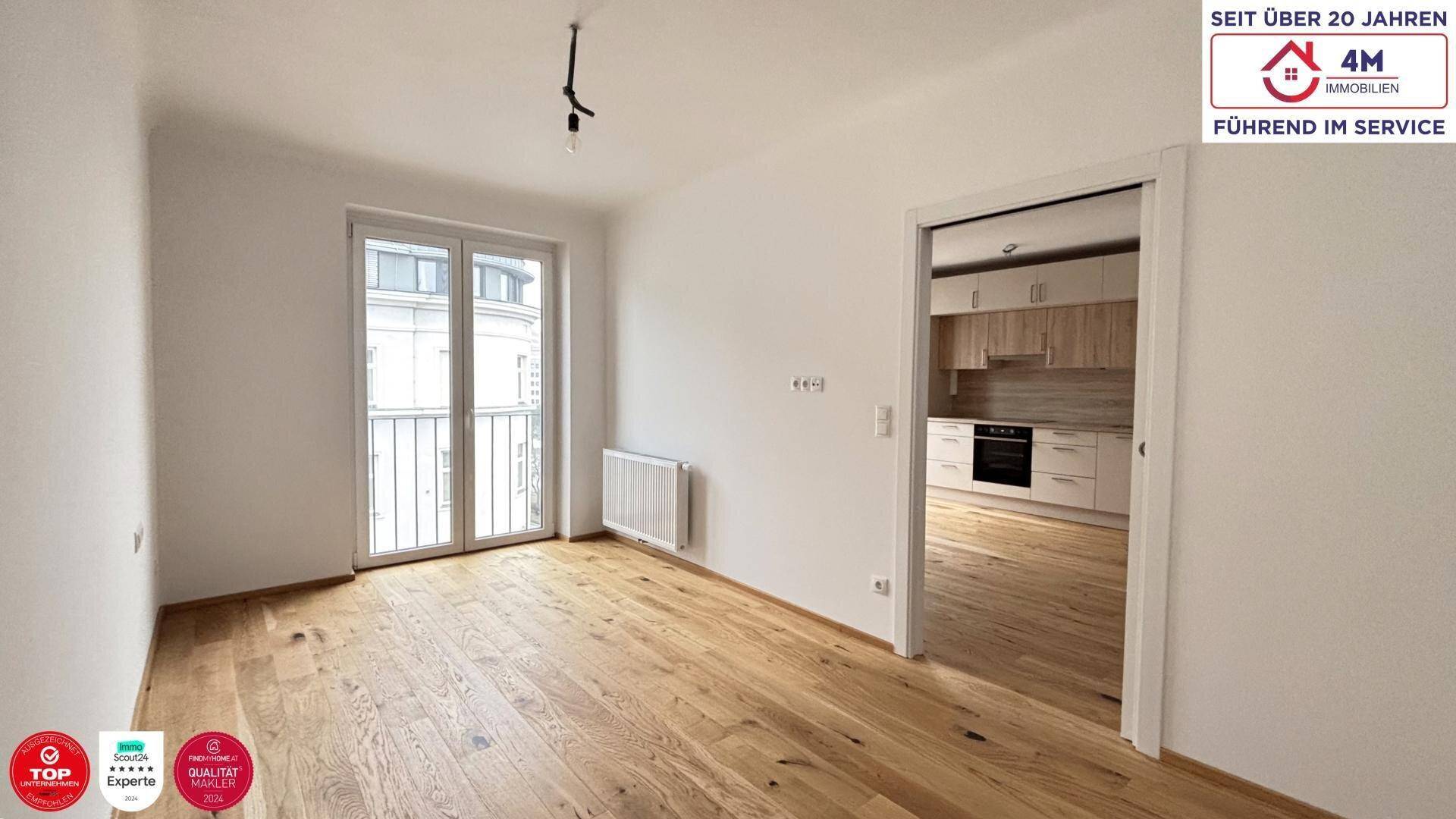 Heller Wohnraum mit Holzboden und Zugang zur Küche, ausgestattet mit einem französischen Balkon.