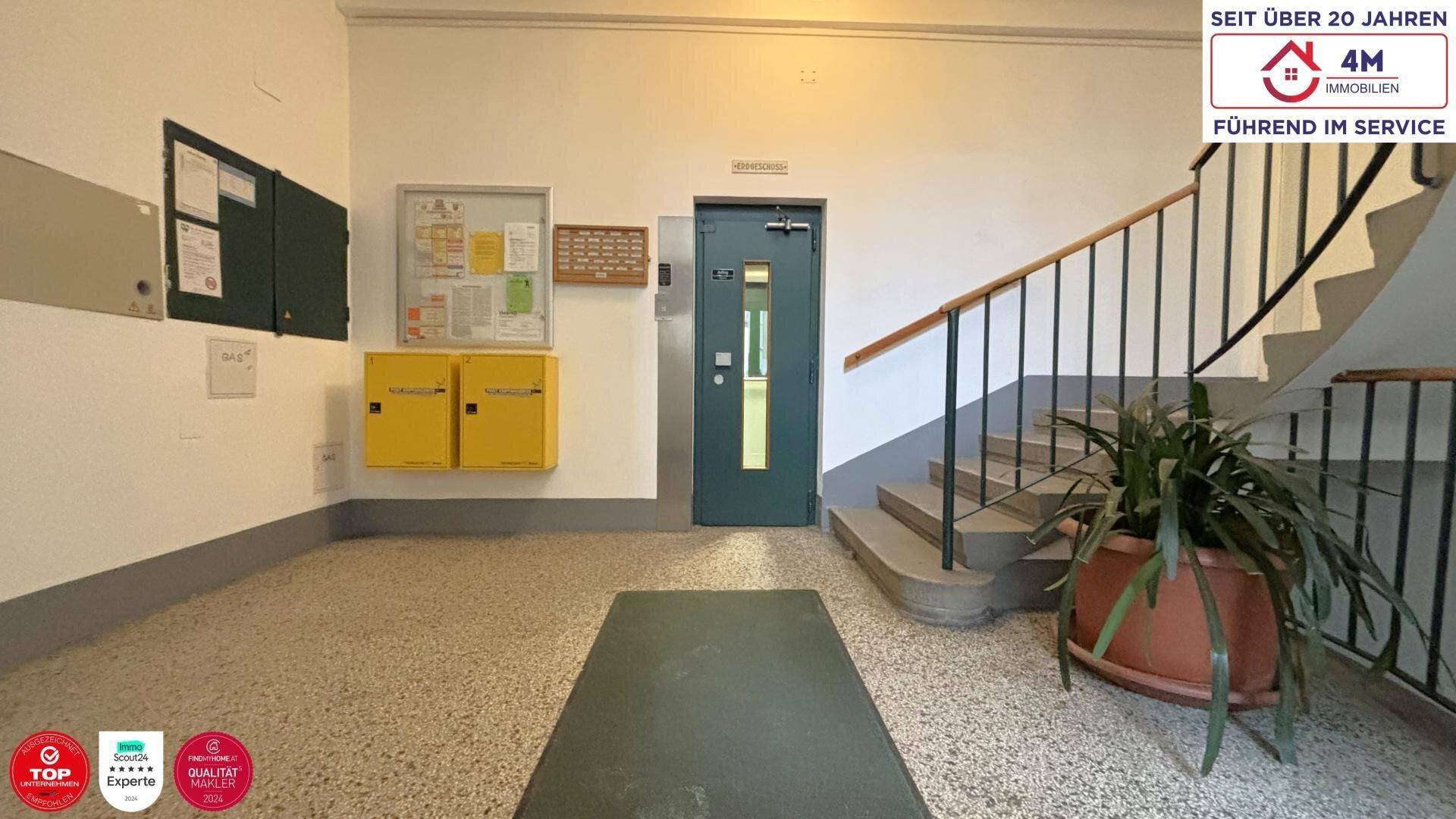 Eingangsbereich eines Gebäudes mit Treppenhaus, Briefkästen und Haustür.