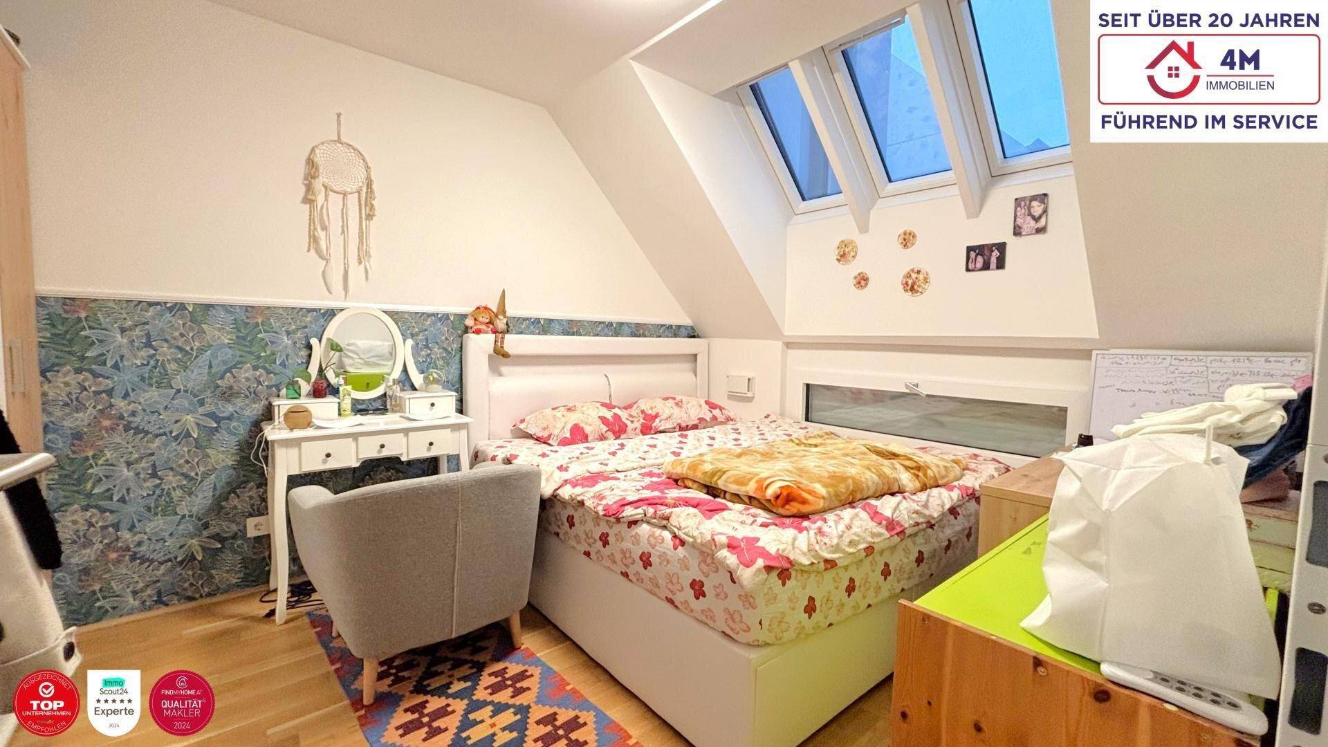 Helles Schlafzimmer mit Dachschräge, Doppelbett und Schminktisch unter großen Dachfenstern.