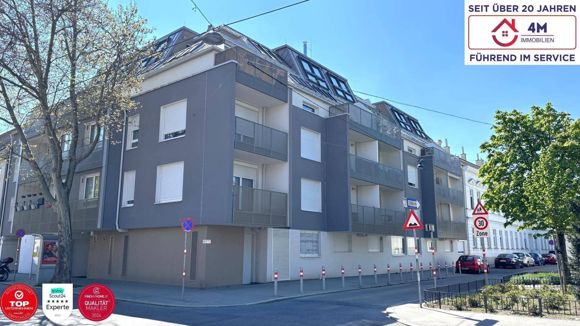 Modernes Mehrfamilienhaus mit grauer Fassade, Balkonen und großen Fenstern in städtischer Umgebung.