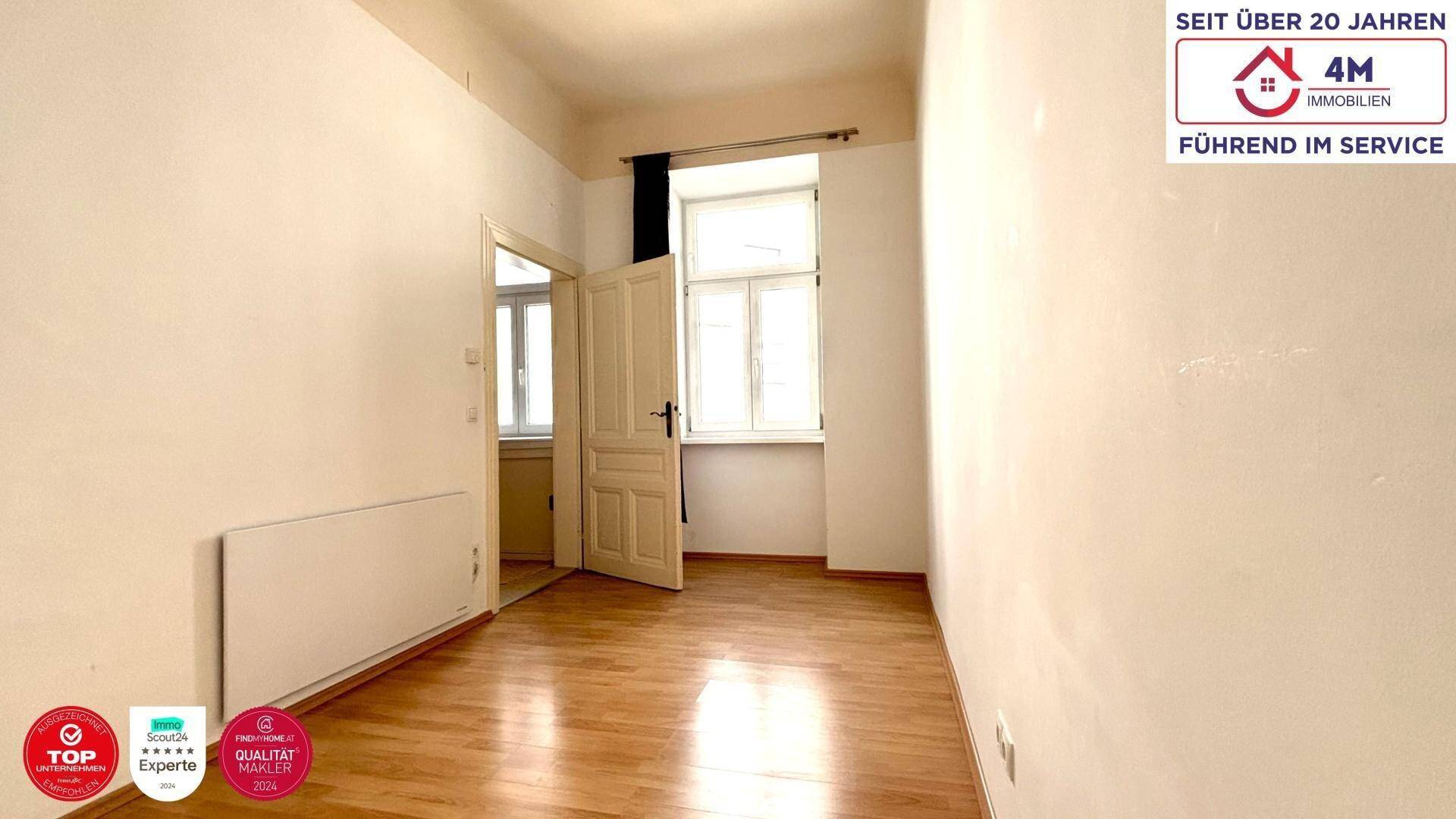 Leeres Zimmer mit Parkettboden, Heizkörper und Zugang zu einem weiteren Raum.