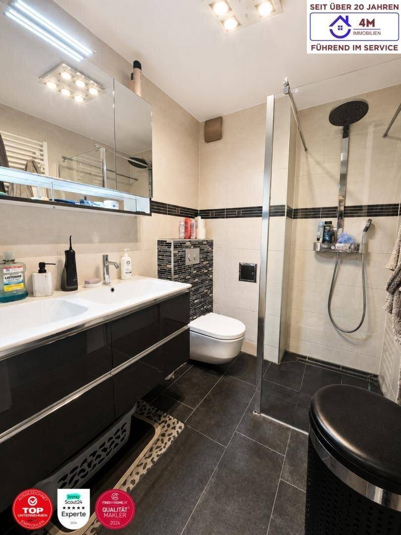 Modernes Badezimmer mit Doppelwaschbecken, Dusche und dunklen Fliesen.