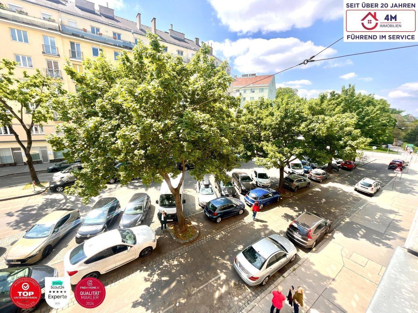 Blick von oben auf eine belebte Straße mit parkenden Autos und Bäumen.