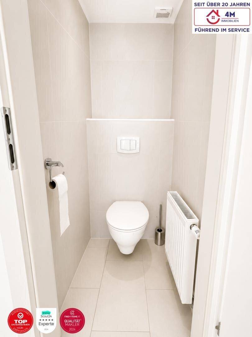 Kleines separates WC mit Wand-WC, Heizkörper und hellen Fliesen.