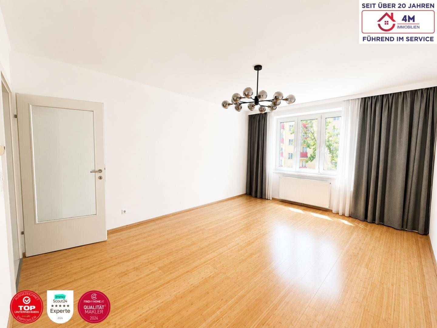 Geräumiges Wohnzimmer mit Holzboden, großen Fenstern und moderner Deckenleuchte.