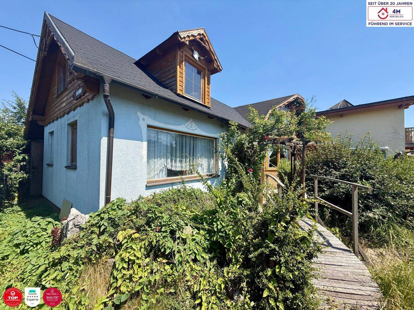 Charmantes Haus mit Holzakzenten und einem kleinen Holzsteg, eingebettet in einen grünen Garten.