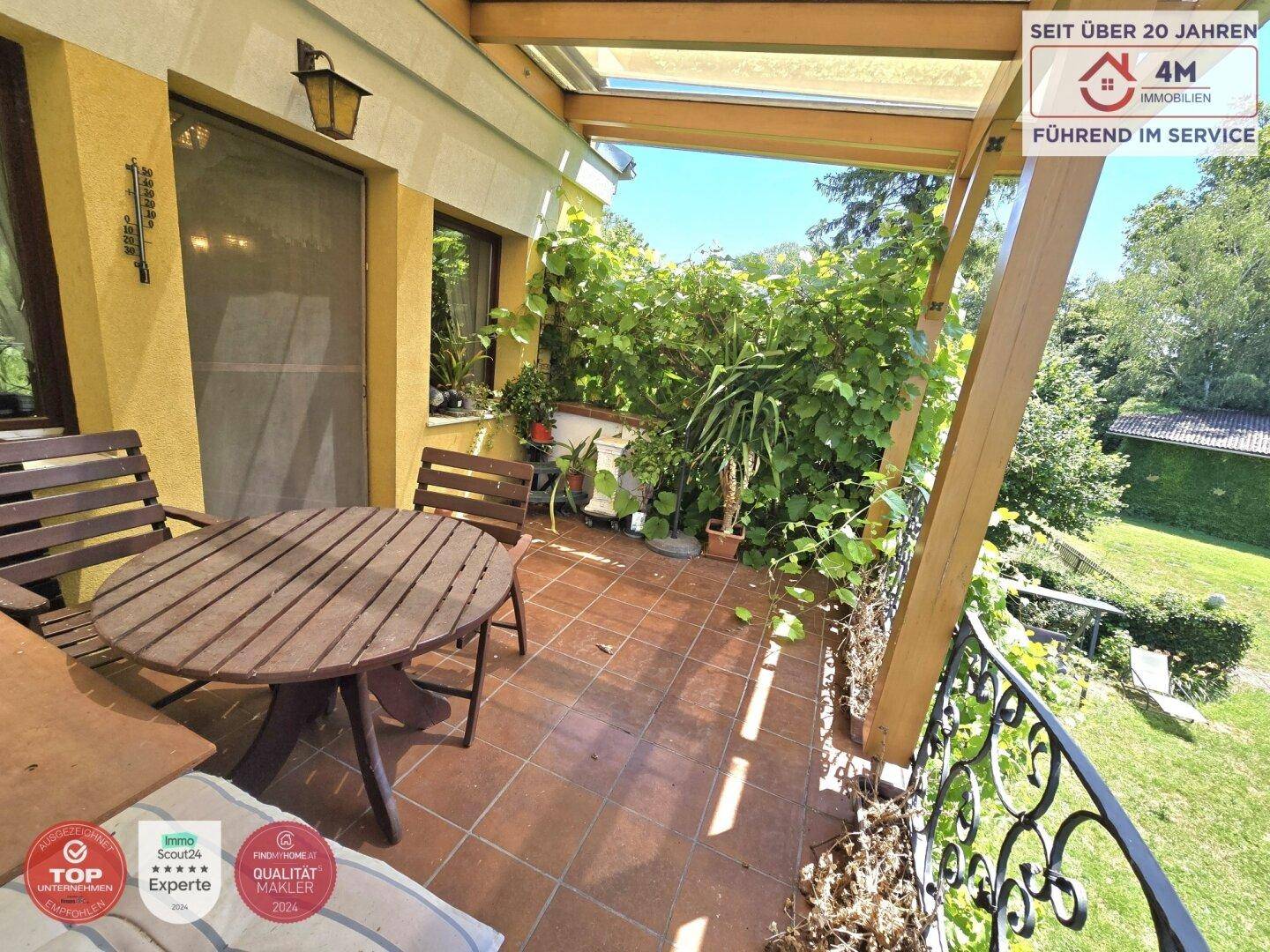 Überdachter Balkon mit Terracotta-Fliesen, Gartenmöbeln und üppiger Bepflanzung.