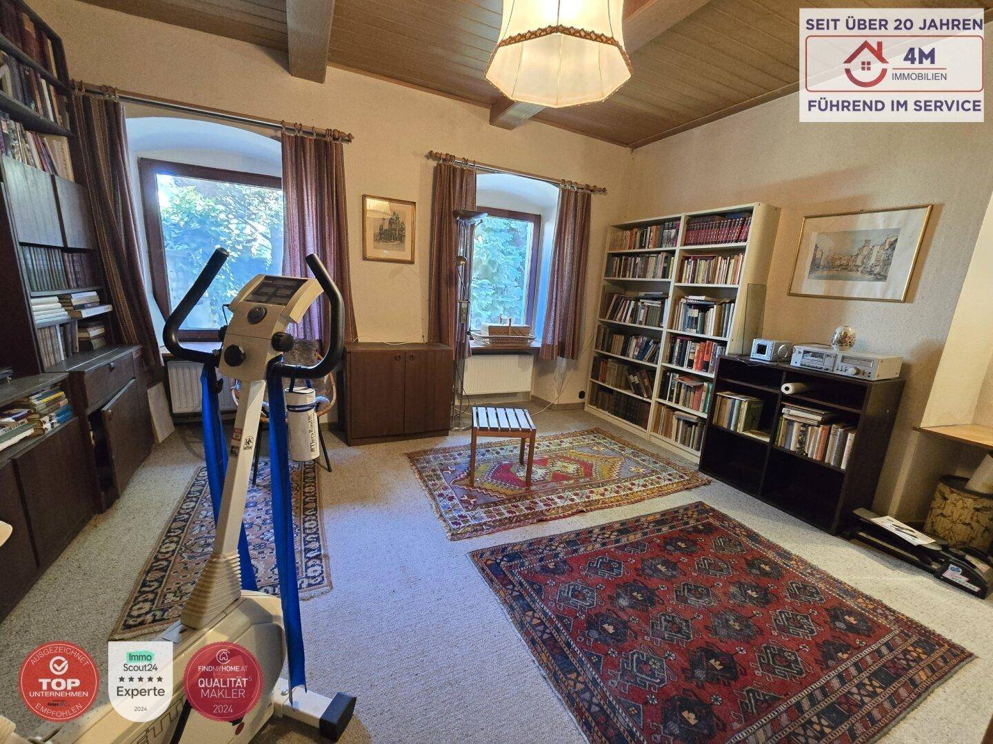 Vielseitiger Raum mit Bücherregalen, Fitnessgerät und Teppichen, genutzt als Büro oder Hobbyraum.