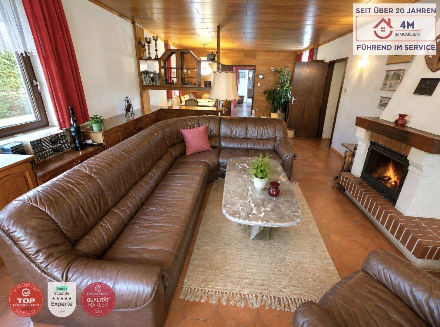 Gemütliches Wohnzimmer mit großem Ledersofa, Kamin und Holzbalkendecke.