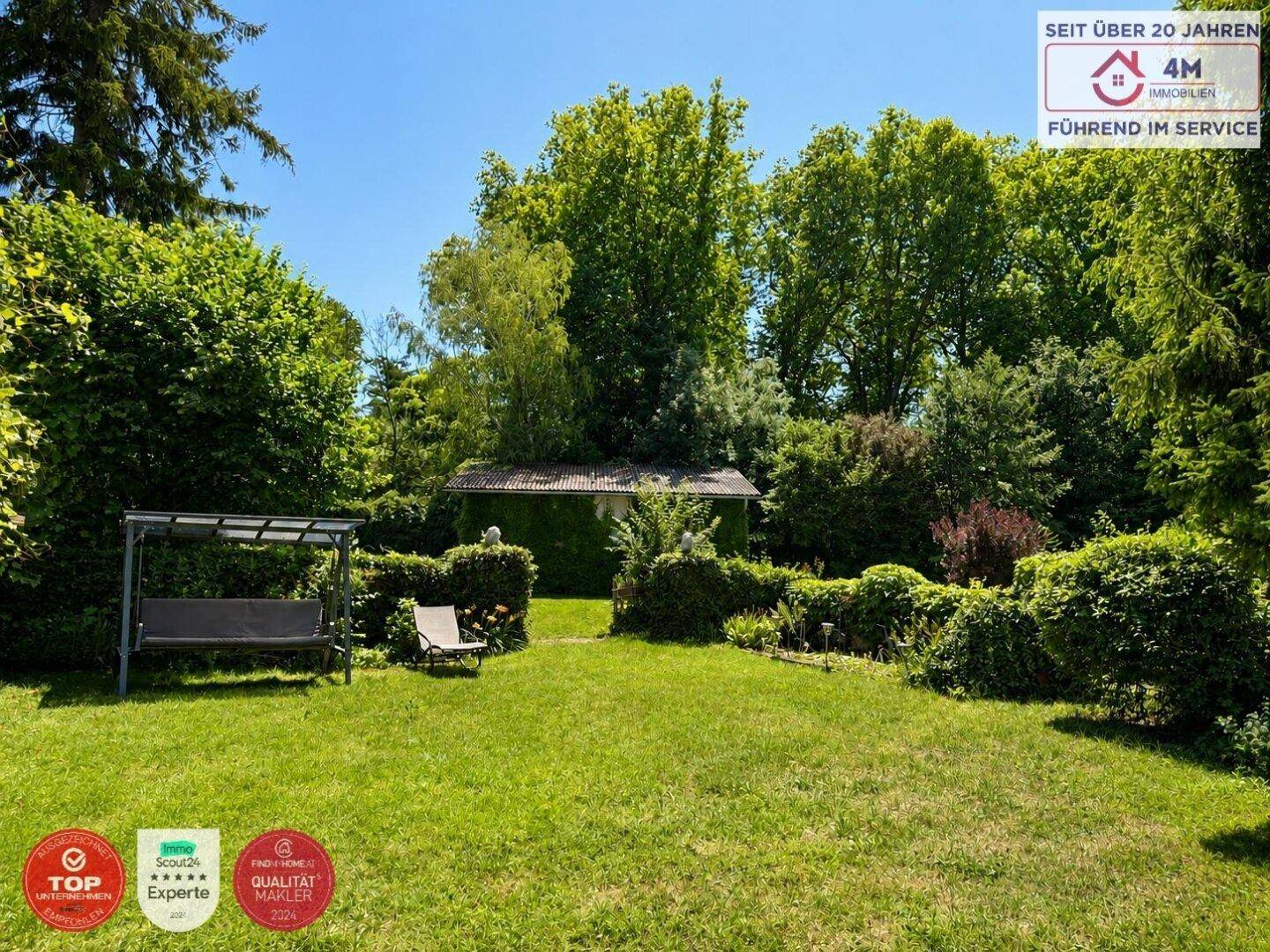 Weitläufiger Garten mit Schaukelbank, Rasenfläche und üppiger Bepflanzung im Hintergrund.