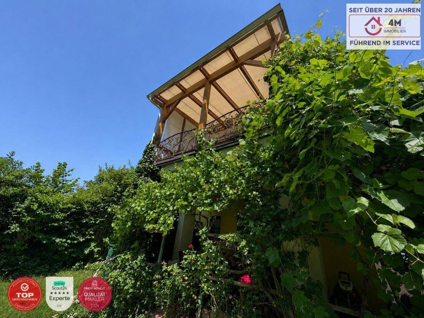 Überwachsener Balkon mit Holzkonstruktion und üppiger Vegetation an der Hausfassade.