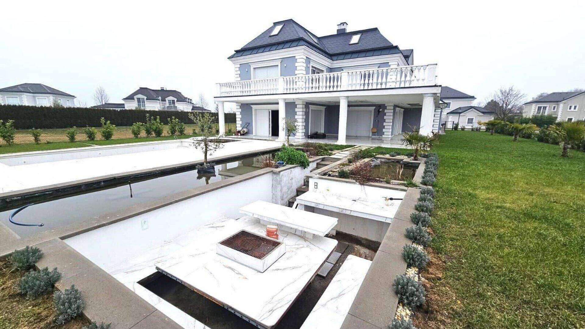 Rückseite der Villa mit großzügigem Garten, Poolbereich und weitläufiger Terrasse mit Säulen.