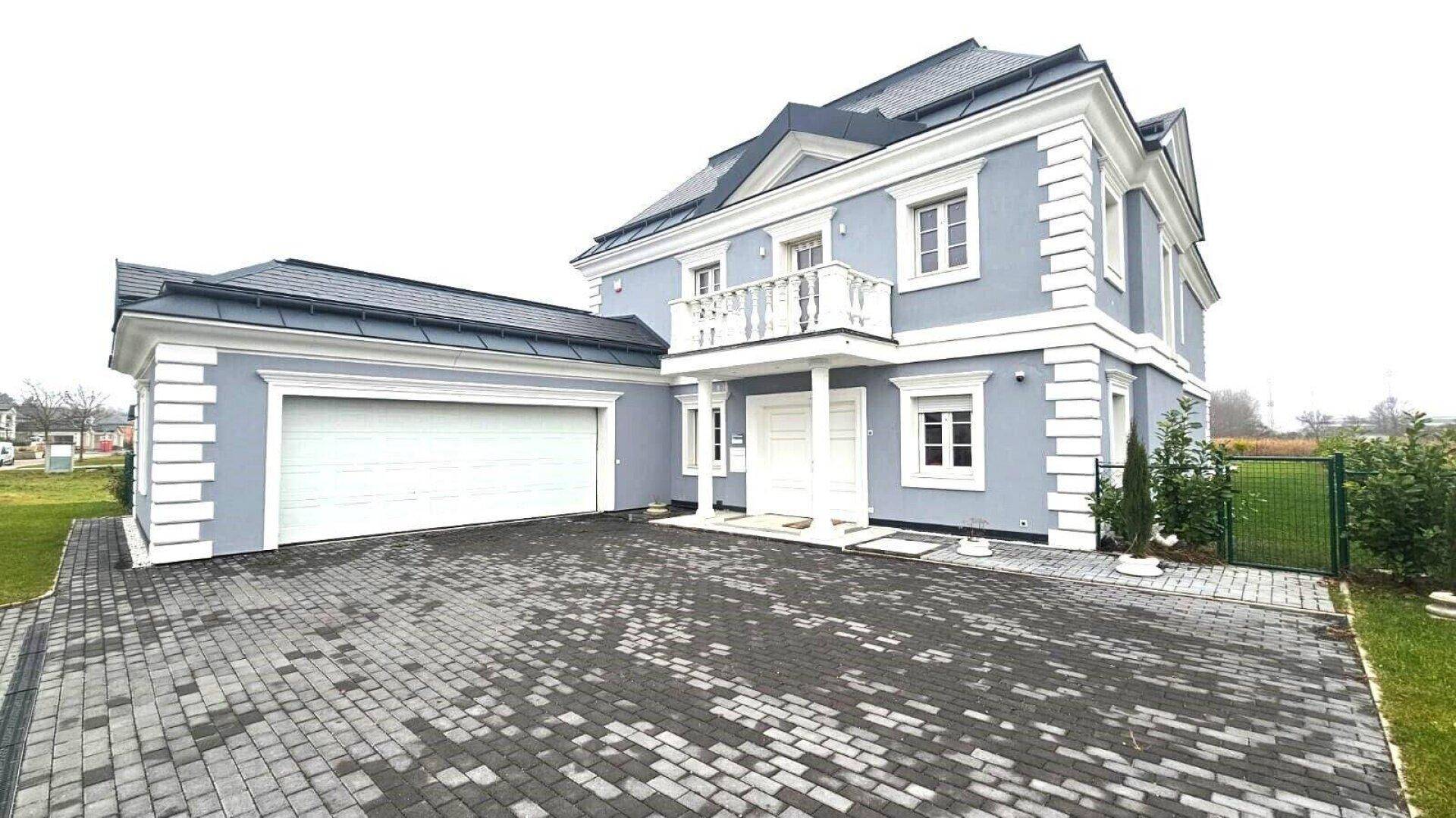 Vorderansicht der modernen Villa mit gepflasterter Auffahrt und integrierter Doppelgarage.