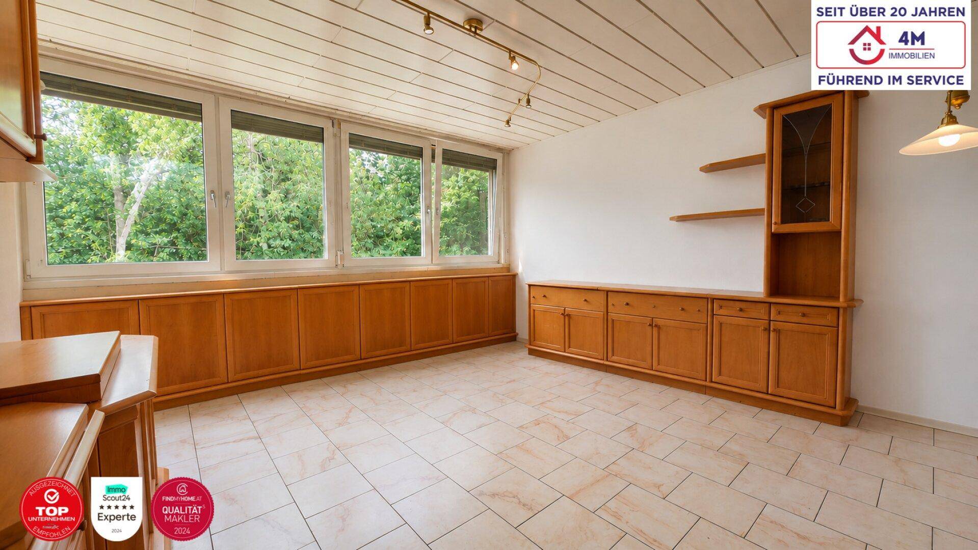 Heller Wohnraum mit großen Fenstern, Holzvertäfelung und Blick ins Grüne.