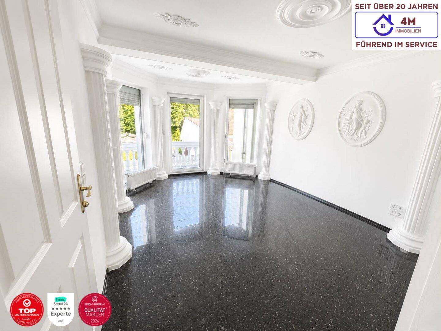 Heller Raum mit dunklem Granitboden, klassischen Säulen und Zugang zu einem Balkon.