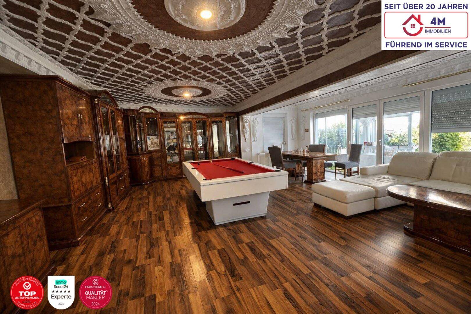 Großzügiger Wohnbereich mit Billardtisch, eleganten Holzmöbeln und dekorativer Decke.