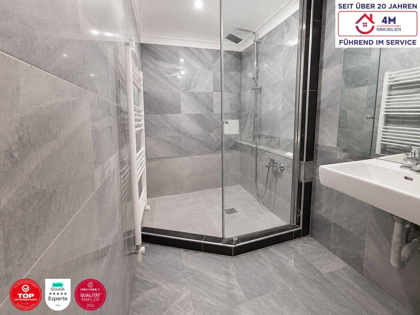 Modernes Badezimmer mit grauen Fliesen, begehbarer Dusche und beheiztem Handtuchhalter.