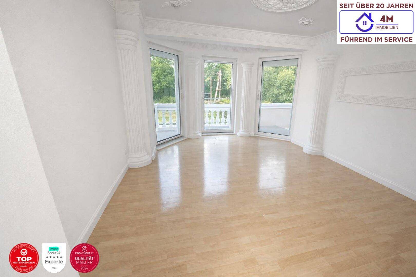 Heller Raum mit hellem Laminatboden, klassischen Säulen und Zugang zu einem Balkon.